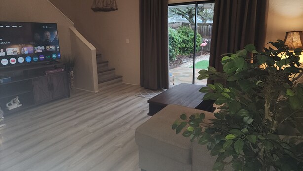 A living room with a flat-screen TV, a staircase, a sliding glass door leading to a patio, and a potted plant.