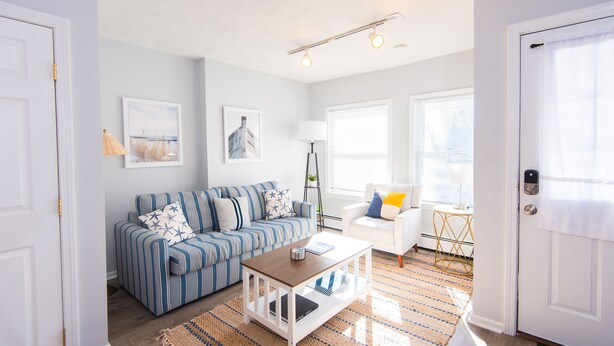 Ein Wohnzimmer mit einem gestreiften Sofa, einem weißen Sessel, einem Couchtisch und einer Lampe.