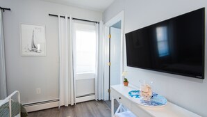 Ein Hotelzimmer mit Bett, Fernseher, Schreibtisch mit Vase und Teller, Fenster mit Vorhängen und einem gerahmten Bild an der Wand.