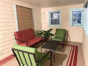 A small patio area with a red sofa, a green armchair, and a table. There is a potted plant and a window with a view. - Newly Renovated 2 BR downtown Apt, family getaway. (Montclair)