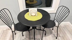 A round black table with a yellow placemat, surrounded by four black metal chairs.