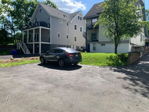 A residential area with a two-story house featuring a balcony and a car parked in the driveway.