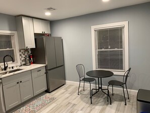 Una cocina con armarios grises, un refrigerador negro, un fregadero y una zona de comedor con una mesa y sillas.