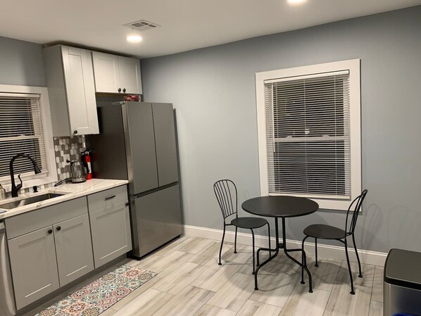 A kitchen with grey cabinets, a black refrigerator, a sink, and a dining area with a table and chairs.
