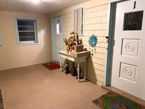Un pasillo con una puerta marcada con el número 1, una mesita con objetos decorativos y un ventanal con marco azul.