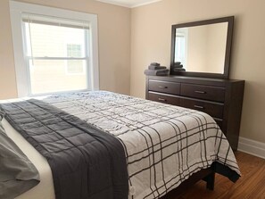 Un dormitorio con cama, cómoda, espejo y ventana.