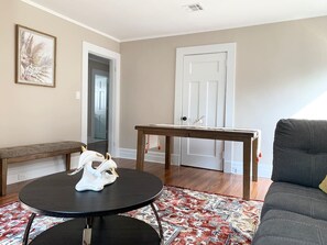 A living room with a round table, a bench, a sofa, a patterned rug, and a door.