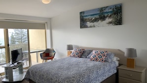 A bedroom with a bed, two bedside lamps, a TV, and a painting on the wall. - Sea Eagles 10 Steps To Kings & Shelly Beach (KINGS BEACH)
