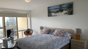 A bedroom with a bed, two bedside lamps, a TV, and a painting on the wall.