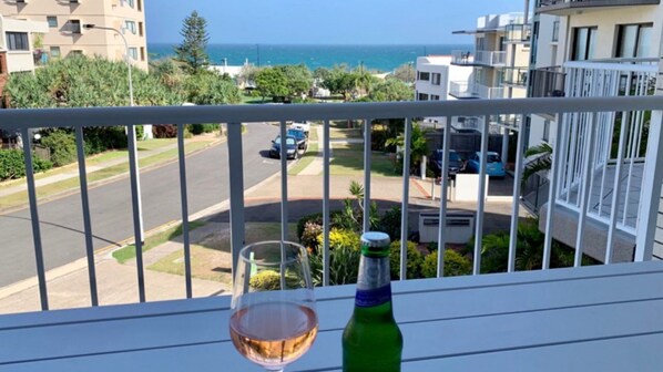Un balcón con una copa de vino y una botella, con vistas a una calle con coches y edificios.