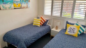 Een slaapkamer met twee eenpersoonsbedden, elk met een stippenbedekking, een nachtkastje met een lamp en een raam met jaloezieën.