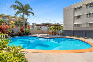 A swimming pool with a patio area, surrounded by palm trees and other greenery. - Edmund Shores 6 Walk To Kings Beach, Ocean Views (KINGS BEACH)