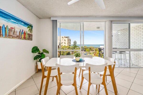 A modern dining area with a round table and chairs, large windows with a view of the sea, and a ceiling fan. - Edmund Shores 6 Walk To Kings Beach, Ocean Views (KINGS BEACH)