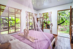 A room with a bed, a wooden bench, a mosquito net, and a view of greenery outside. - Playa Ganadito Ecolodge (Drake Bay)