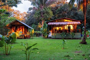 Two wooden cabins with thatched roofs surrounded by lush greenery. - Playa Ganadito Ecolodge (Drake Bay)