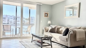 A hotel room with a large sliding glass door leading to a balcony, a sofa with a throw blanket, a small table, and a lamp. - FABULOUS WATERFRONT STUDIO APT IN ST PETE FL! (Saint Petersburg)