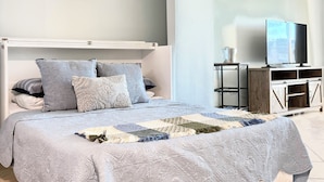 A neatly arranged bedroom with a bed, bedside table, and a television on a stand. - FABULOUS WATERFRONT STUDIO APT IN ST PETE FL! (Saint Petersburg)