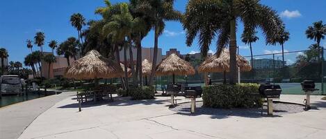 A beachfront area with palm trees, thatched umbrellas, and a concrete walkway.