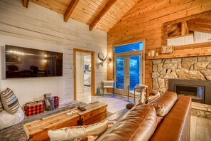 Interior acogedor de una cabaña de madera con chimenea de piedra, sofá de cuero y un televisor grande montado en la pared.
