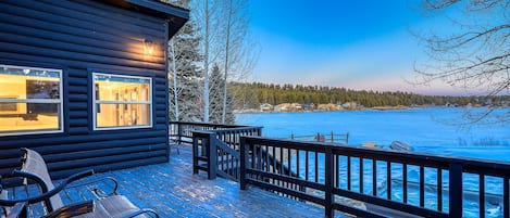 Guests can enjoy a serene lakeside view from the cabin's deck, which features comfortable seating and two windows with warm interior lighting.