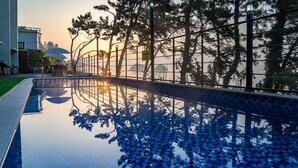 A pool with a clear reflection of trees and a fence, surrounded by a well-maintained lawn and a building with a balcony. - Yeosu Sea&blue Family Pension (Yeosu)