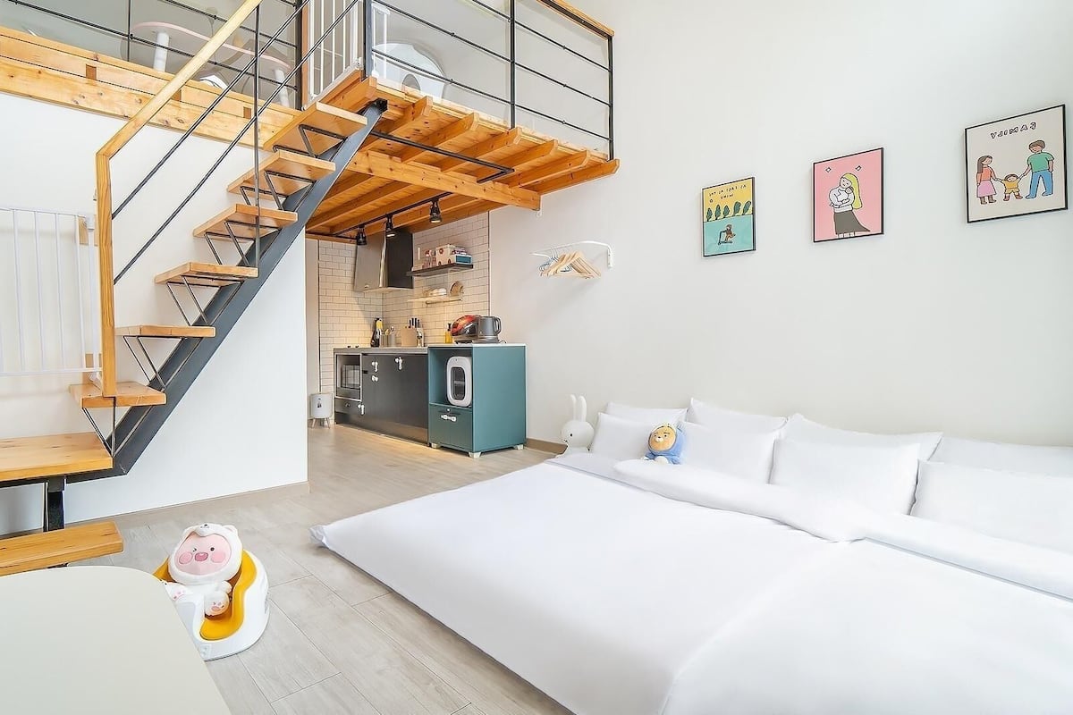 A modern apartment with a wooden staircase, a kitchen, a dining area, and a bedroom.