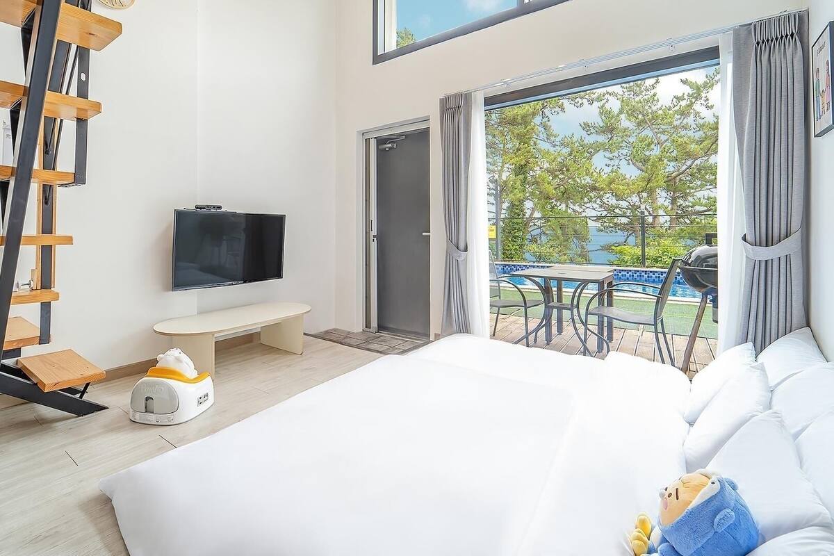 A bedroom with a bed, a TV, a bench, a bedside table, and a view of a pool.