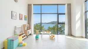 A spacious room with a large window, a play area with toys, a bed, and a view of the sea. - Yeosu Sea&blue Family Pension (Yeosu)