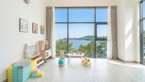 A spacious room with a large window, a play area with toys, a bed, and a view of the sea.