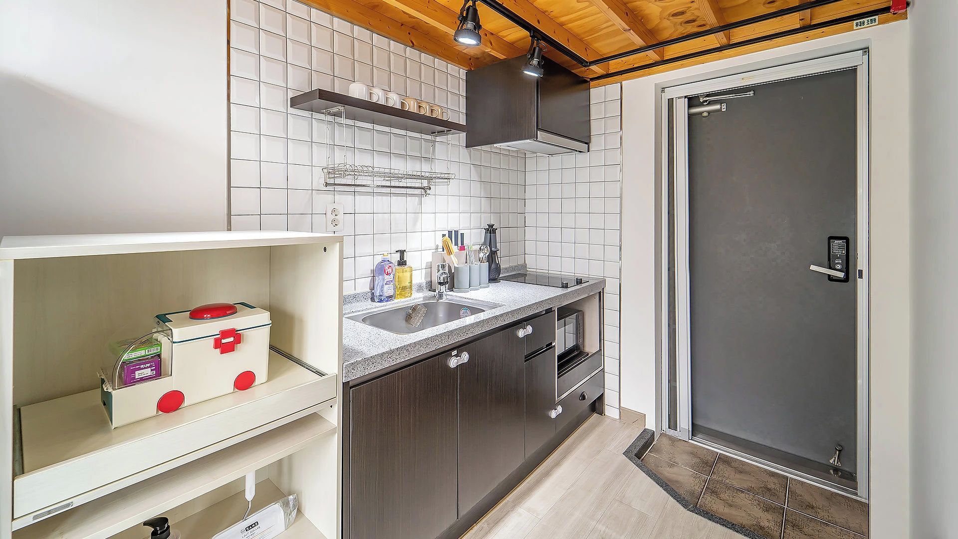 A compact kitchen with white tiled backsplash, a built-in sink, and a door leading to a bathroom.