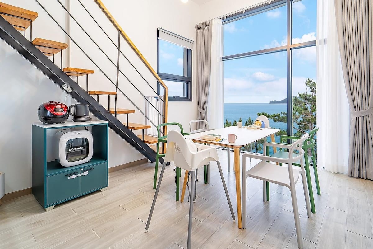 A modern interior with a dining area, a staircase, and a view of the sea.