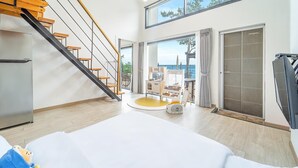 A modern hotel room with a wooden staircase, a bed, a small seating area, and a view of the sea. - Yeosu Sea&blue Family Pension (Yeosu)