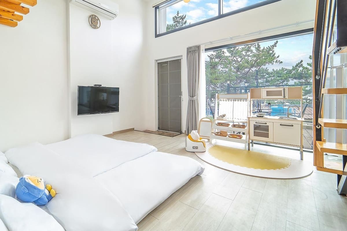 A bedroom with a large bed, a TV, and a sliding glass door leading to a balcony with outdoor furniture.