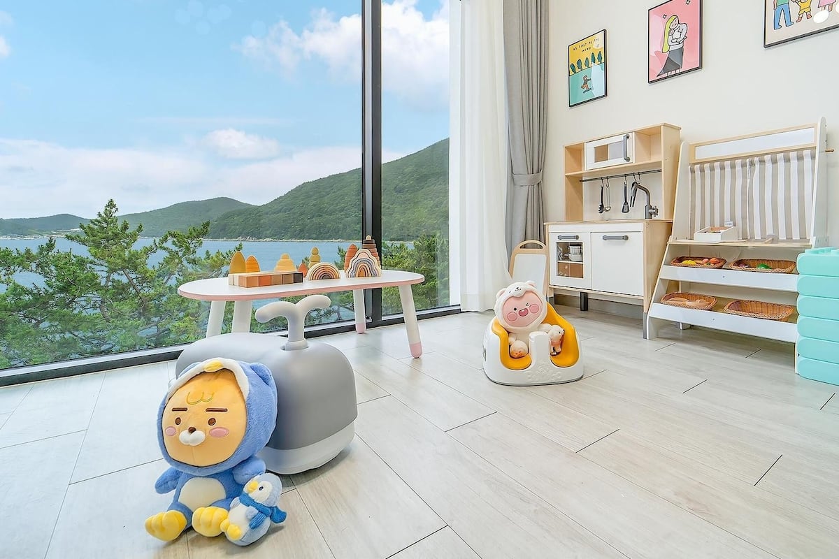 A child's play area with toys, a view of the sea, and a large window.