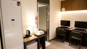 A hotel room with a refrigerator, a desk with a computer, two chairs, a lamp, and a fire extinguisher. - Chungjangro 1st Boutique Hotel (Gwangju)