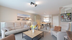 Un salon moderne comprenant un canapé, un fauteuil, une table basse et un coin repas avec une table et des chaises.