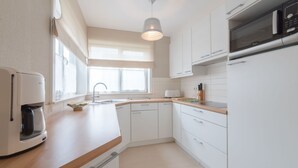 Une cuisine moderne avec des armoires blanches, un plan de travail en bois, un four à micro-ondes encastré et une machine à café.