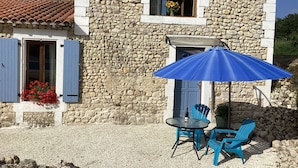 A stone building with a tiled roof, a window with a blue shutter, and a patio area with a table and chairs. - Chez Goret Gites - Gite Skippy  Couples only (Nouvelle- Aquitaine)