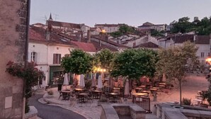 Una strada acciottolata che conduce a un cortile con posti a sedere all'aperto, circondato da edifici dall'architettura tradizionale.