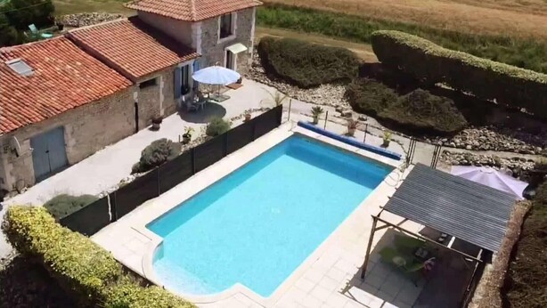 Una piscina rettangolare con bordo piastrellato, circondata da un basso muro in pietra e un siepe.