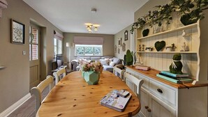 Uma sala de jantar com uma mesa de madeira, cadeiras, um vaso com flores e uma estante com objetos decorativos.