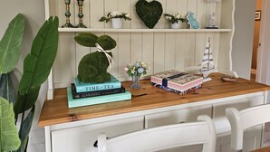 Uma mesa de madeira com uma pilha de livros, uma planta decorativa e uma pequena estatueta.