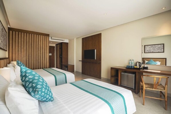 Habitación de hotel con dos camas, un escritorio, un televisor y un refrigerador pequeño.