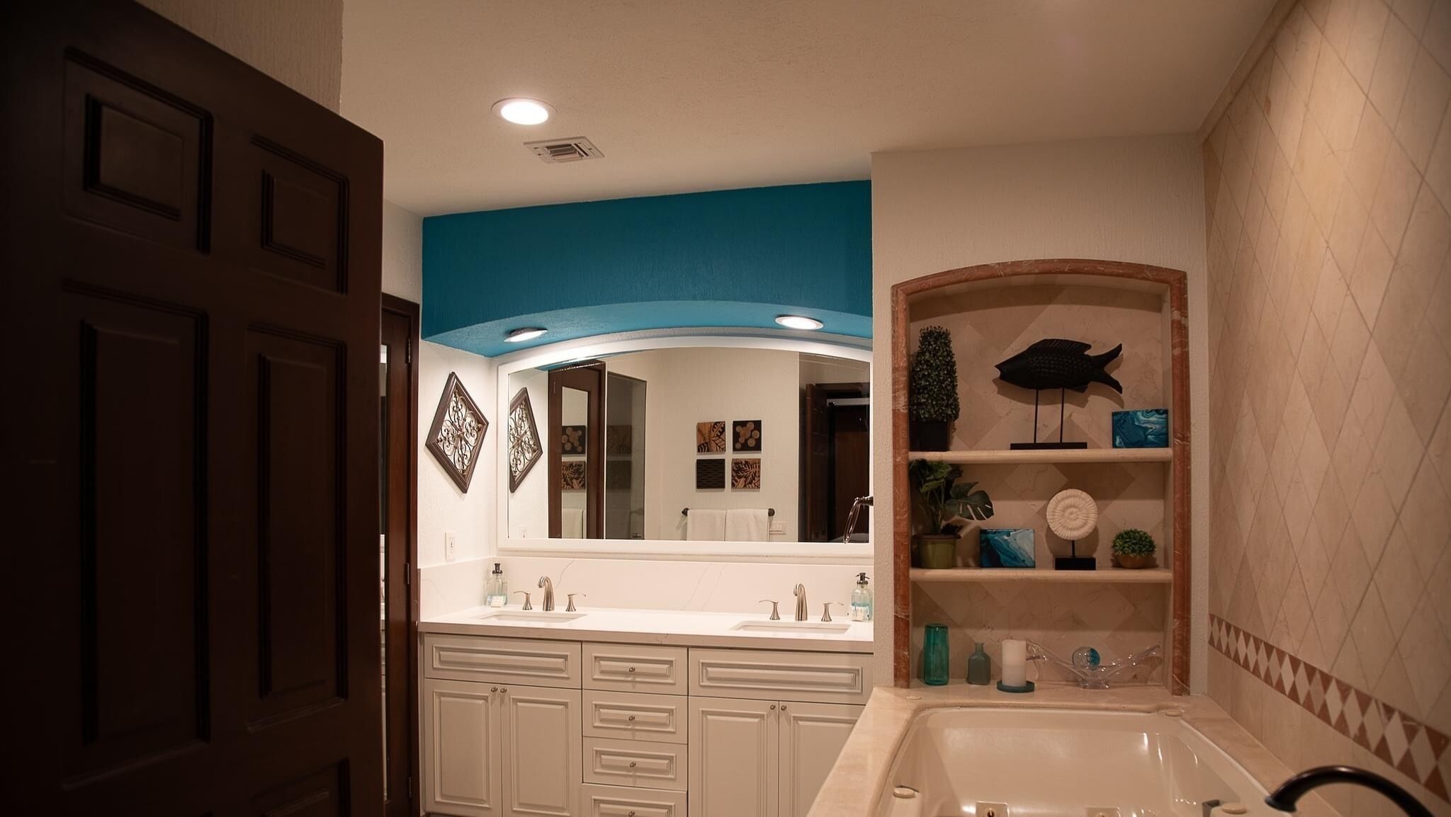 Une salle de bain avec un meuble-lavabo blanc, un grand miroir et une étagère ornée d’objets décoratifs.