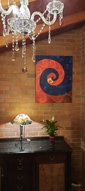 Um quarto com parede de tijolos, um lustre, um quadro, um abajur e uma planta.