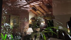 Une pièce avec un mur en briques, un plafond en bois et une grande fenêtre qui reflète les plantes.
