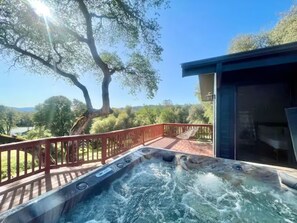 A hot tub on a deck with a view of trees and a clear sky.