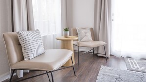 Due sedie con cuscini decorati, un piccolo tavolino rotondo con una pianta e un tappeto su un pavimento in legno.