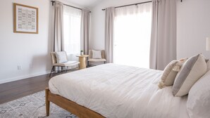 Una camera da letto moderna con un letto grande, due poltrone, un tavolino e un'ampia finestra con tende.