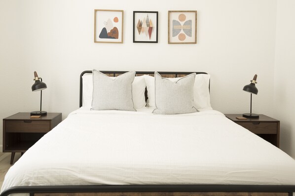 A neatly made bed with white bedding, two bedside tables with lamps, and three framed artworks on the wall.